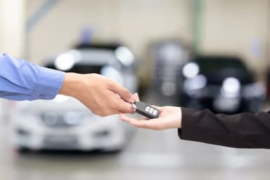 Mão de vendedor entregando uma chave de carro preta na mão de um cliente, mostrando como vender carro automático.