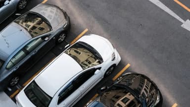 Imagem aérea de carros estacionados em vagas urbanas, com reflexos de prédios, ilustrando gestão de estoque e como calcular custo de carro parado na operação.